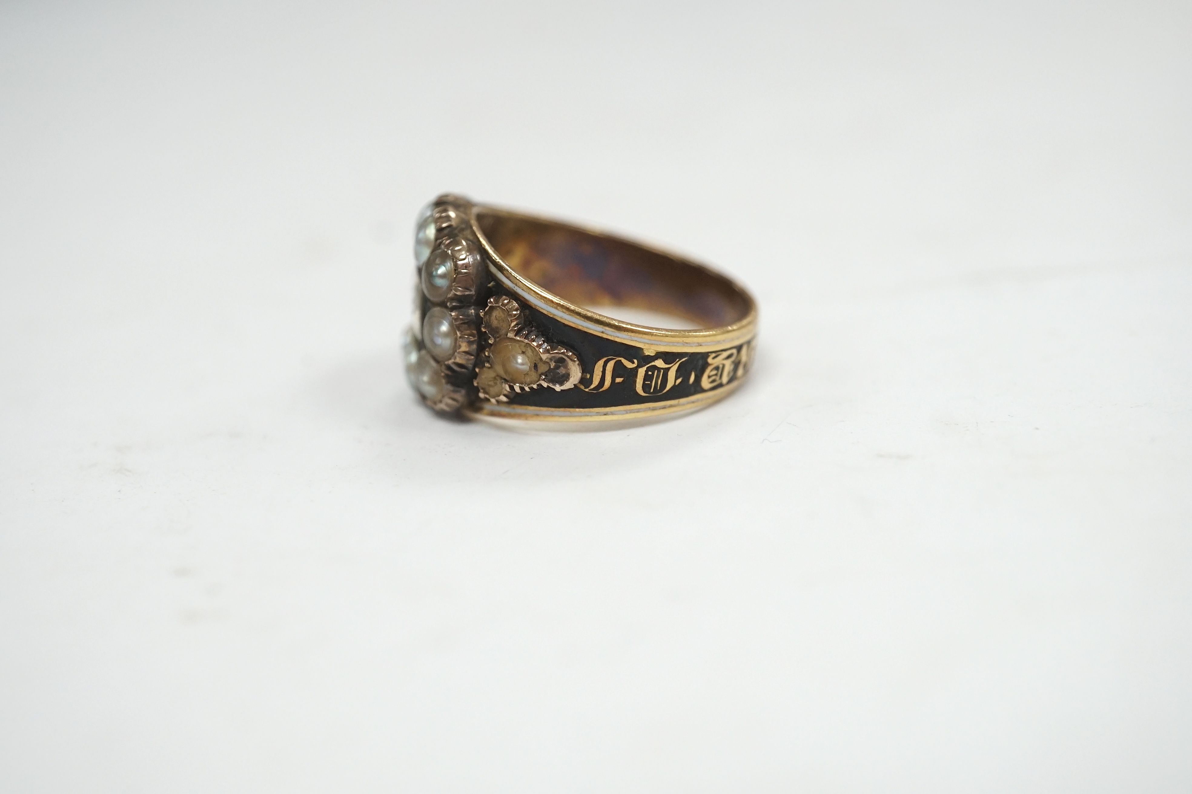 A late George III yellow metal, two colour enamel and split pearl set mourning ring, with plaited hair beneath a glazed panel, inscribed, 'M.J. Escott died 12th July, 1817 aged 21', size N, gross weight 6.8 grams. Condit